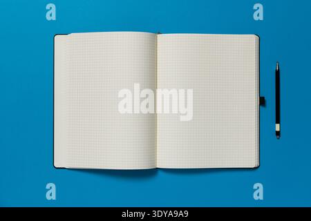 Open notepad on a blue  background. The page is blank and there is pen on the side. Stock Photo