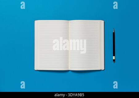 Open notepad on a blue  background. The page is blank and there is pen on the side. Stock Photo