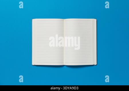 Open notepad on a blue background. The page is blank. Stock Photo
