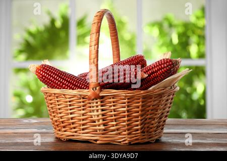 Red corn cobs in basket on wooden table indoors Stock Photo