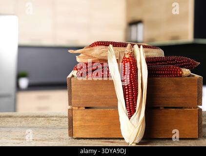 Red corn cobs in crate on wooden table in kitchen Stock Photo
