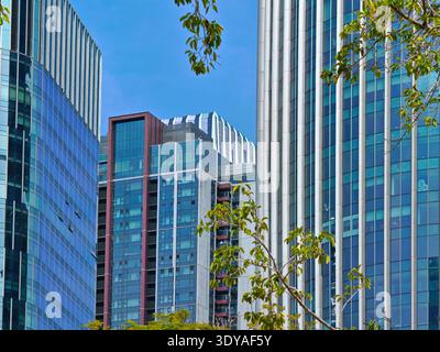 A high-resolution close-up of a bustling cityscape featuring sleek, reflective glass and metal skyscrapers against a clear, bright blue sky. The build Stock Photo