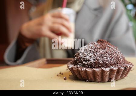 Chocolate muffin on a table with a drink in hand Stock Photo