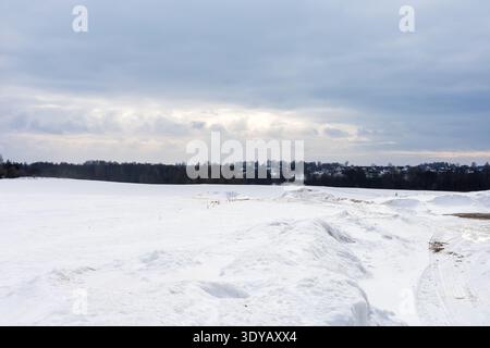 Snowy field under overcast sky, distant trees on horizon, rolling snowdrifts creating textured foreground leading Stock Photo
