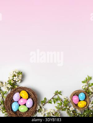 Easter colored painted eggs in bird nests and blooming spring cherry branches on pink background with space for text and greetings. Easter and spring concept. Spring background Stock Photo