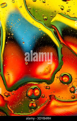 Striking macro photography of iridescent oil bubbles on a multi color background featuring saturated red, yellow and blue liquid gradients. Stock Photo