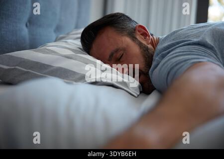 Sleeping, fatigue and man on bed for peace, burnout crash and mental exhaustion for weekend relaxing. Tired, resting and mature person comfortable in Stock Photo
