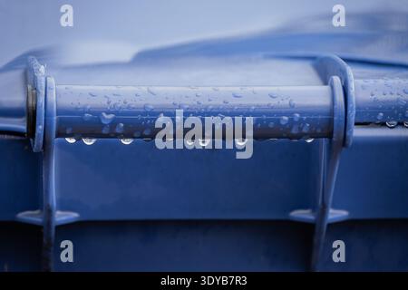 Macro view of crystal clear raindrops hanging from a blue plastic handle after rainfall. Focus on water surface tension and detail Stock Photo