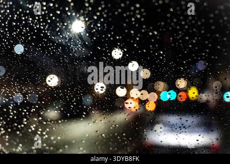 Nighttime abstract of raindrops on a car windshield with colorful out-of-focus city lights and traffic bokeh Stock Photo