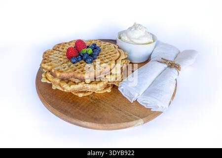 Heart-shaped Swedish waffles with fresh blueberries, raspberries and whipped cream on a wooden board Stock Photo