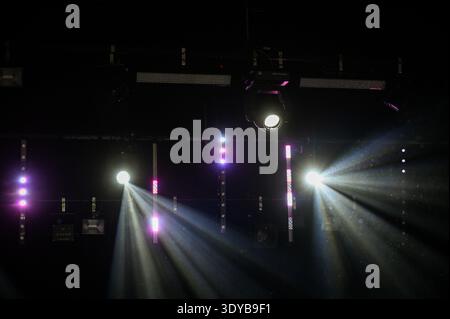 Powerful stage spotlights casting bright beams through haze in a dark concert venue. Professional lighting rig with LED bars creates dramatic atmosphe Stock Photo