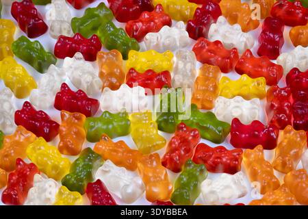 Vibrant multicolored gummy bears create abstract scattered background, glossy candy shapes forming energetic color field ideal for modern design, wall Stock Photo