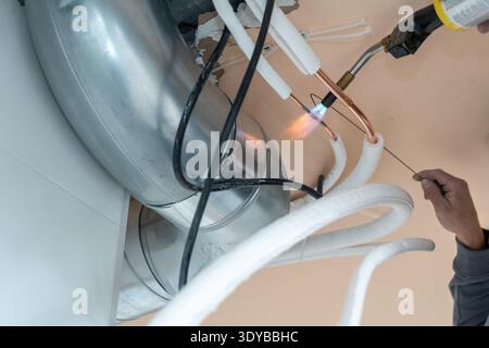 Technician installing a modern hvac system, using a blowtorch to braze copper pipes for an air conditioning unit, ensuring proper function and heating Stock Photo