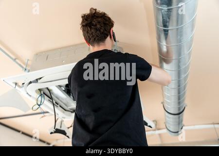 Technician installing air conditioning ceiling unit and ductwork Stock Photo