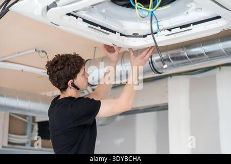 Technician installing ceiling air conditioning unit during construction Stock Photo
