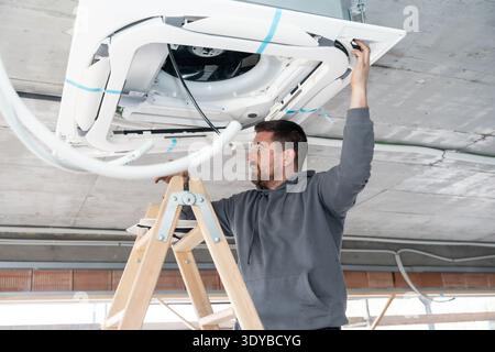 Hvac technician installing air conditioning system on new construction ceiling Stock Photo