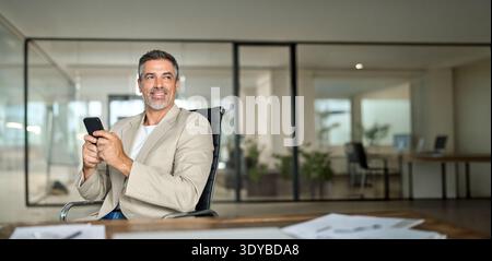 Happy middle aged business man wearing suit using phone in office looking away. Stock Photo