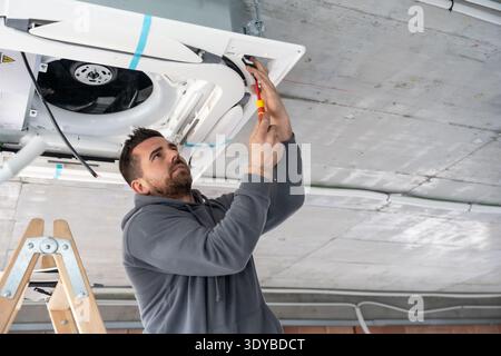 Hvac technician installing air conditioning ceiling unit in building Stock Photo
