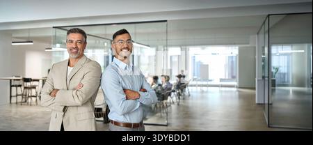 Two happy business partners standing back to back in corporate office. Portrait. Stock Photo