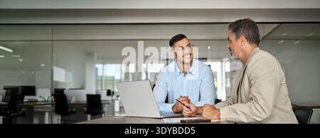 Young smiling latin business man working in office with executive using laptop. Stock Photo