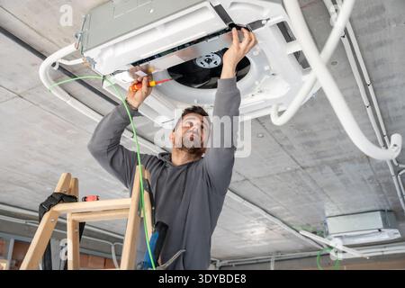Air conditioning technician installing ventilation system on a building ceiling Stock Photo
