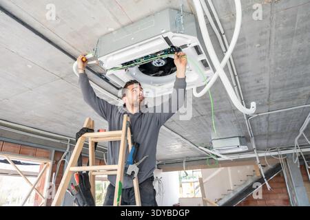 Air conditioning technician installing hvac system on ceiling Stock Photo