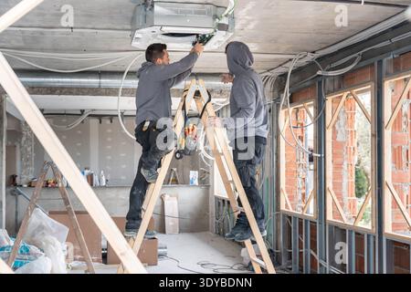 Technicians installing air conditioning unit on construction site Stock Photo