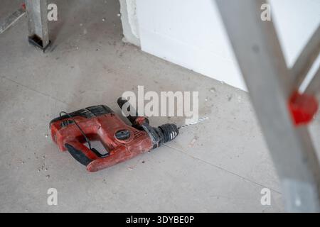 Rotary hammer drill lying on a dusty concrete floor in a room under renovation, indicating ongoing construction, demolition, drilling, and building ac Stock Photo