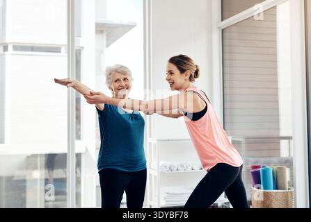 Old woman, help and instructor in yoga class, stretching and happiness for technique. Trainer, retirement activity and people in facility, exercise Stock Photo