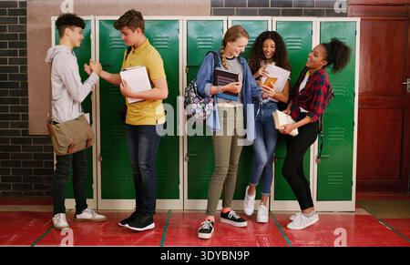 Locker, handshake and friends with phone in school, discussion and academy app for lesson timetable. Teenager, boys and happy girls with mobile for Stock Photo