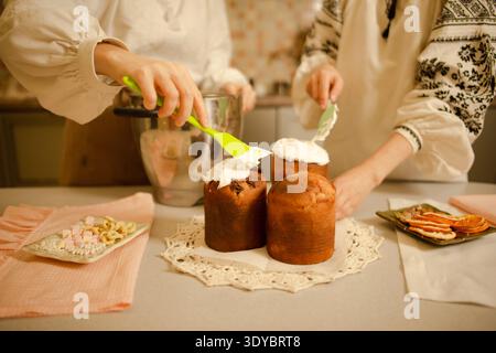 women decorate traditional Easter pastries, covering tops of Easter cakes with egg white icing Stock Photo