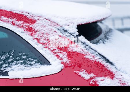 Close up of red car roof and rear window covered with fresh snow and melting droplets, urban winter parking detail, cold weather commute concept, sele Stock Photo