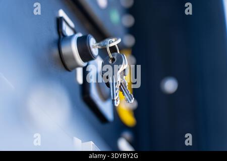 Close up of keys inserted in metal lock switch on machine panel, blue toned industrial background with bokeh, access control, security and maintenance Stock Photo
