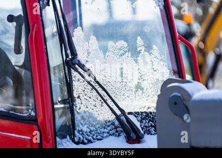 Ice coated front window of heavy equipment cab with wipers and snow buildup, detailed winter texture on glass, showing visibility risk, deicing needs Stock Photo