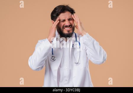 30s aged physician man in white medical coat form having headache, studio portrait. Guy putting hands on head, isolated on warm yellow background. Concept of problems, medicine, illness High quality || Model released Stock Photo