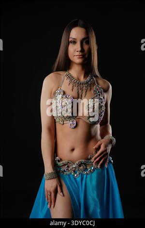 A woman stands in a dark space, dancing with a snake. She wears a decorated outfit and showcases her movement. The setting highlights her performance and the snake's presence in the act. || Model released Stock Photo