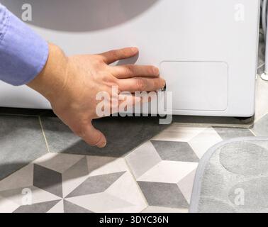 Man opening the drain pump filter access panel of the front loading washing machine Stock Photo