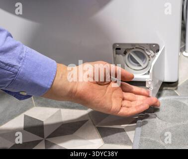 Man opening the drain pump filter access panel of the front loading washing machine Stock Photo