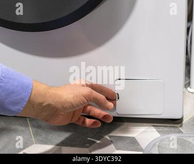 Man opening the drain pump filter access panel of the front loading washing machine Stock Photo