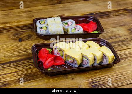 Set of sushi rolls in plastic boxes on wooden table. Sushi for take away or delivery of sushi in plastic containers Stock Photo