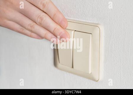 Hand pressing light switch on white wall, controlling power Stock Photo