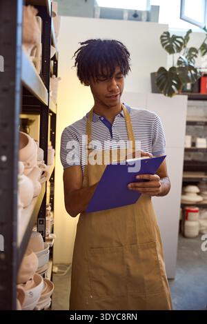 Young man writing on clipboard in pottery studio during daytime Stock Photo