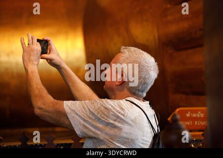 BANGKOK, THAILAND-FEB 7, 2026: Senior man taking photo with smartphone inside temple, mobile photography during travel experience, side profile Stock Photo