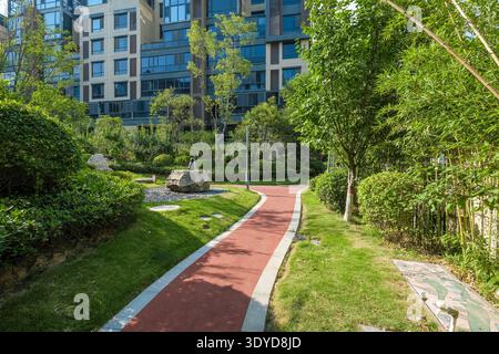 A horizontal landscape view of a red brick jogging path curving through a lush, tree-filled garden in a modern apartment community. Stock Photo