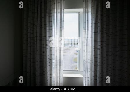 Soft daylight entering through sheer curtains and a tall window in a minimal interior, creating a calm mood around privacy, rest and quiet indoor spac Stock Photo