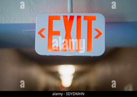 Bright red EXIT sign with directional arrows above a soft focus corridor, representing emergency preparedness, architectural safety guidance and clear Stock Photo