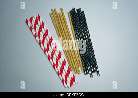 A collection of paper straws in red white stripes brown and black patterns arranged on a light surface for eco friendly drinking options. Stock Photo