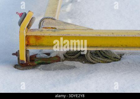 A rusty yellow metal beam lies on snow covered ground with a coiled rope and ice, showing signs of wear and cold weather conditions. Stock Photo