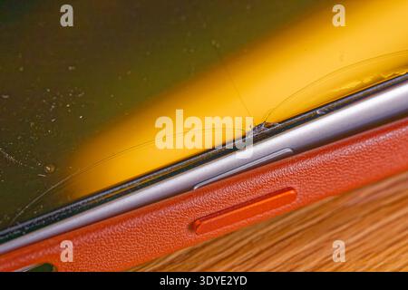 A smartphone with a cracked screen and a textured protective case is shown with visible damage and scratches on the display surface. Stock Photo