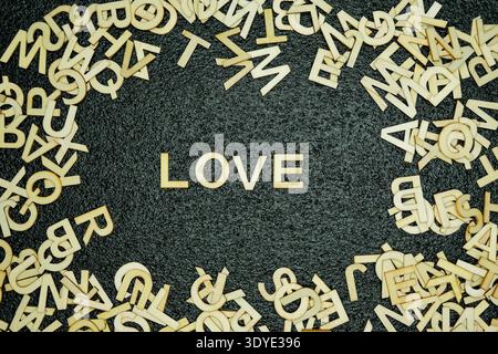 Wooden alphabet letters scattered on a textured black background with the word love spelled out clearly in the center symbolizing affection and commun Stock Photo